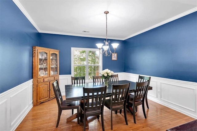 dining area featuring a chandelier, light wood-style flooring, a decorative wall, wainscoting, and crown molding