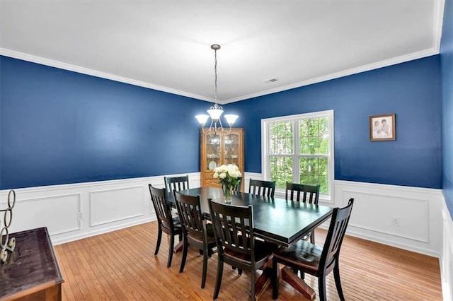 dining area with a wainscoted wall, a chandelier, hardwood / wood-style floors, ornamental molding, and a decorative wall