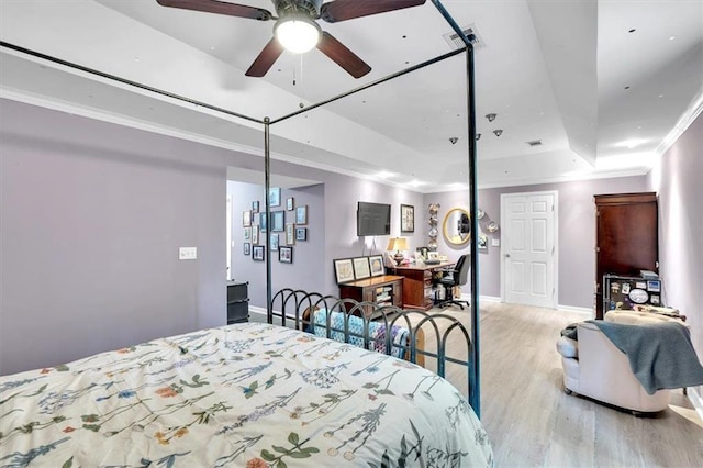 bedroom with a tray ceiling, wood finished floors, ornamental molding, and baseboards