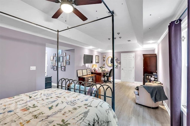 bedroom featuring wood finished floors, baseboards, a tray ceiling, and crown molding