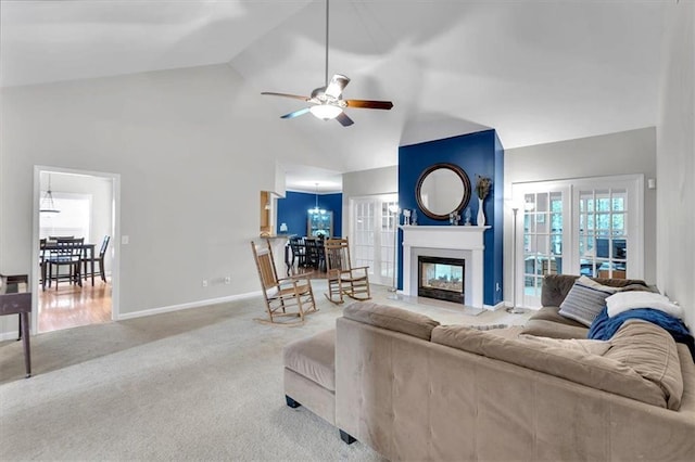 living room featuring vaulted ceiling, a ceiling fan, carpet floors, a glass covered fireplace, and baseboards