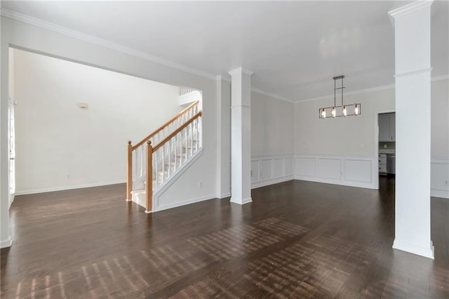 unfurnished living room with crown molding, dark hardwood / wood-style flooring, an inviting chandelier, and ornate columns