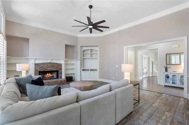 living room featuring built in shelves, crown molding, wood-type flooring, ceiling fan, and a fireplace