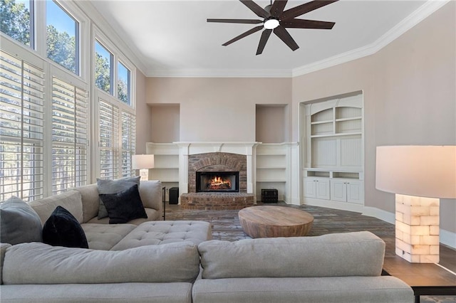 living room with built in shelves, crown molding, a brick fireplace, dark hardwood / wood-style flooring, and ceiling fan