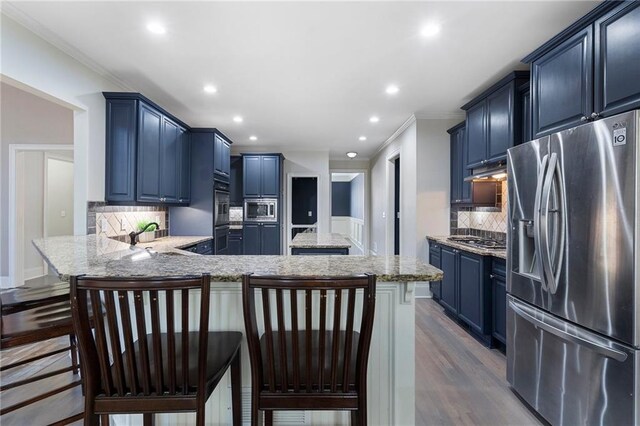 kitchen featuring blue cabinets, appliances with stainless steel finishes, backsplash, and a kitchen breakfast bar