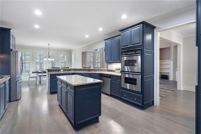 kitchen featuring appliances with stainless steel finishes, pendant lighting, ornamental molding, a center island, and light hardwood / wood-style floors