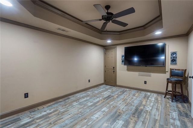 interior space with ceiling fan, ornamental molding, a raised ceiling, and light wood-type flooring