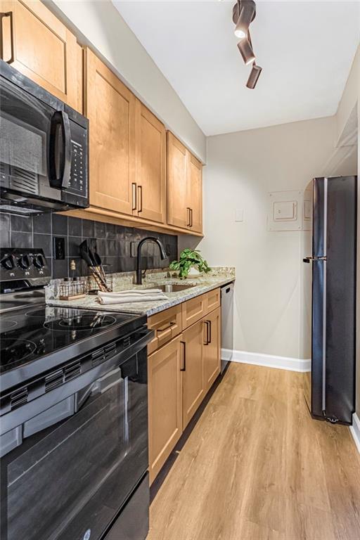 kitchen featuring black appliances, a sink, light wood-style flooring, tasteful backsplash, and baseboards