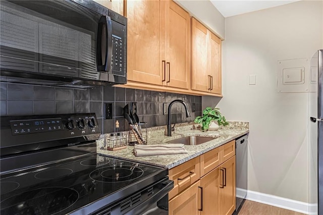 kitchen featuring black appliances, a sink, light stone countertops, and tasteful backsplash