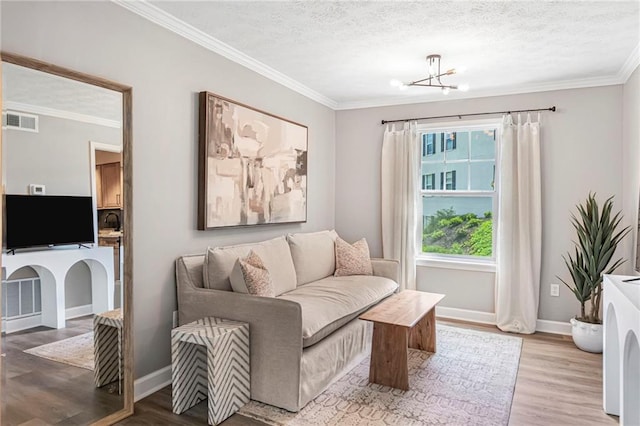 living area featuring ornamental molding, wood finished floors, a chandelier, baseboards, and a textured ceiling