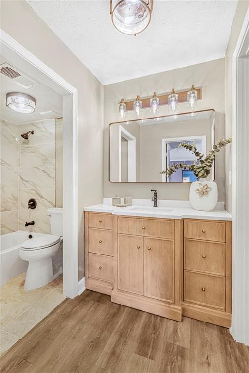 bathroom featuring wood finished floors, vanity, toilet, bathing tub / shower combination, and a textured ceiling
