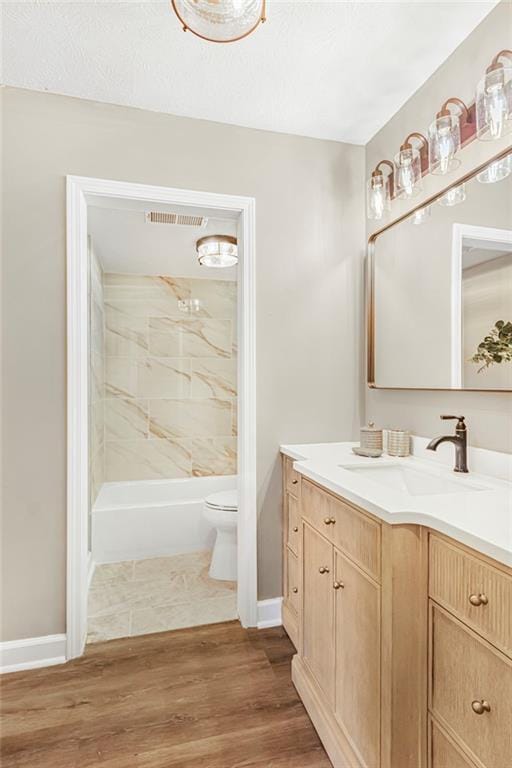 full bath featuring toilet, vanity, wood finished floors, baseboards, and tub / shower combination