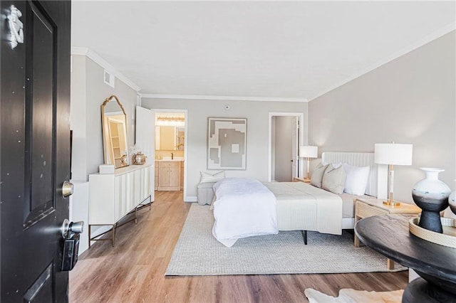 bedroom with light wood-type flooring, ornamental molding, baseboards, and connected bathroom