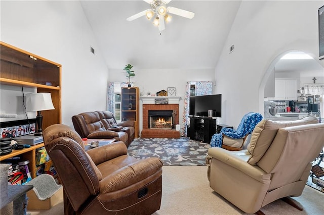 carpeted living room with ceiling fan, a fireplace, and high vaulted ceiling