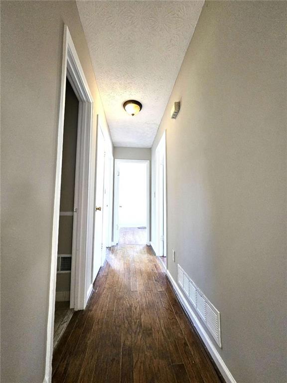 corridor with a textured ceiling and dark hardwood / wood-style floors