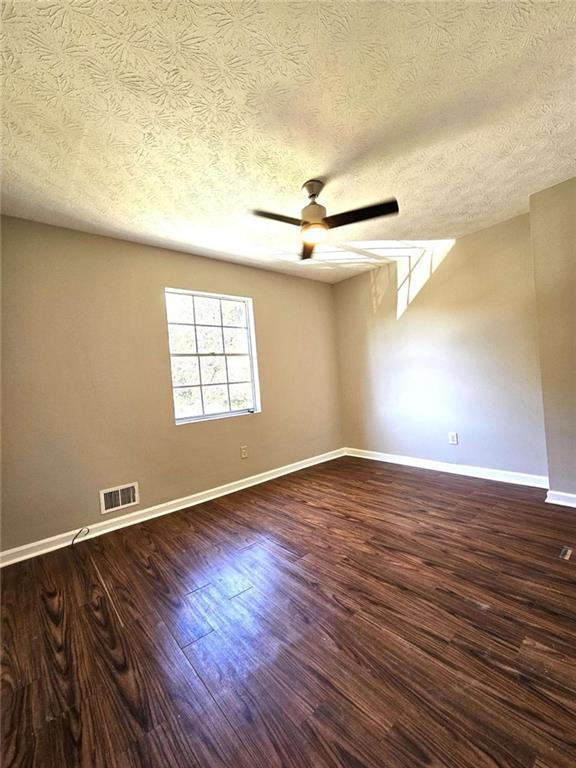 spare room with a textured ceiling, ceiling fan, and dark hardwood / wood-style flooring