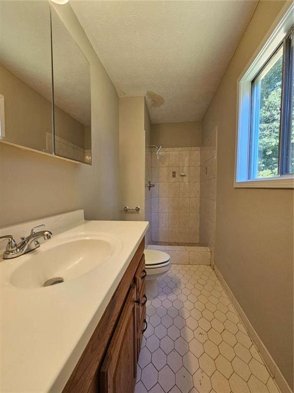 bathroom featuring toilet, a tile shower, tile patterned floors, a textured ceiling, and vanity