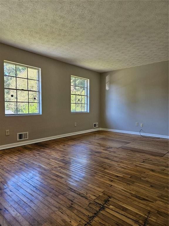 empty room with dark wood-type flooring, a wealth of natural light, and a textured ceiling