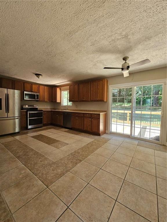 kitchen featuring a textured ceiling, tile patterned flooring, stainless steel appliances, sink, and ceiling fan