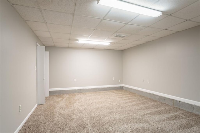 empty room featuring carpet flooring, visible vents, baseboards, and a drop ceiling