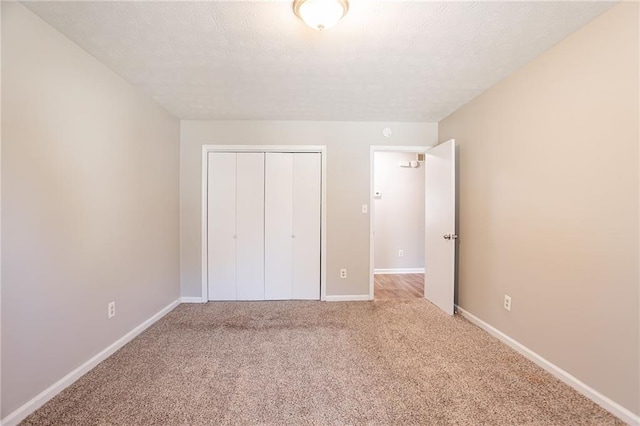 unfurnished bedroom featuring a textured ceiling, light colored carpet, a closet, and baseboards