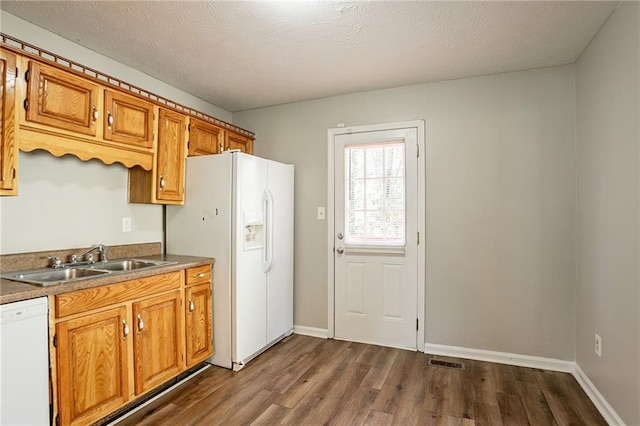 kitchen with white appliances, brown cabinetry, dark wood-style floors, visible vents, and a sink