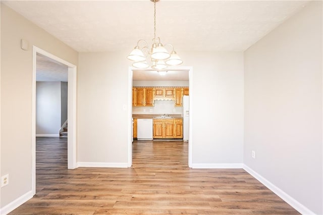 unfurnished dining area featuring a sink, light wood-type flooring, an inviting chandelier, and stairway