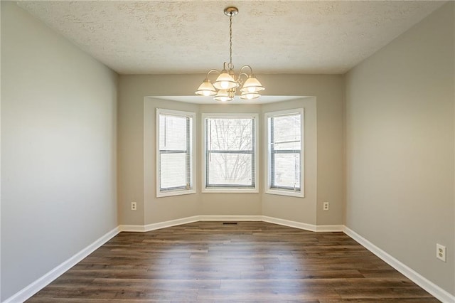 unfurnished room with a textured ceiling, baseboards, an inviting chandelier, and dark wood-style flooring