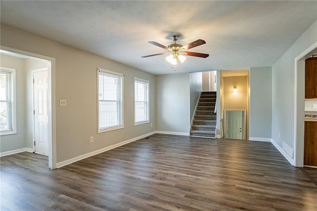 unfurnished living room with a textured ceiling, dark wood-style floors, baseboards, ceiling fan, and stairs