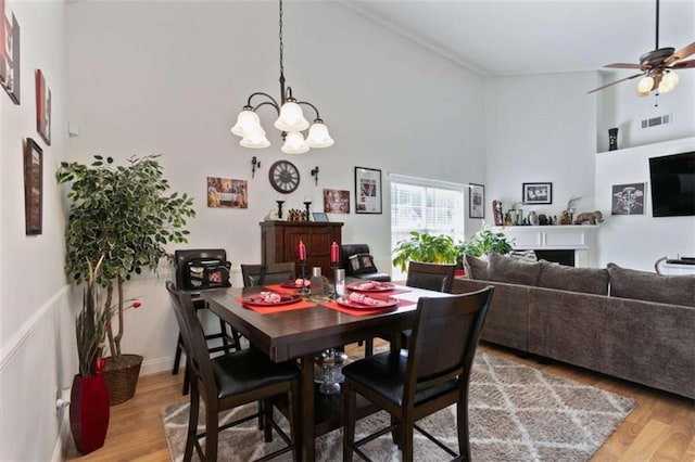 dining area featuring hardwood / wood-style flooring, ceiling fan with notable chandelier, and a high ceiling