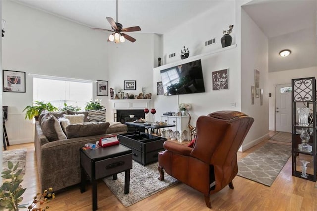 living room with a towering ceiling, ceiling fan, and light hardwood / wood-style flooring