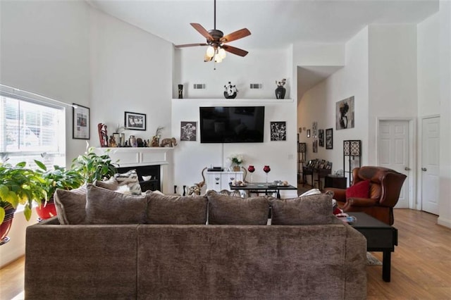 living room featuring a high ceiling, ceiling fan, and light wood-type flooring