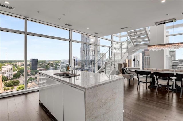 kitchen with sink, white cabinets, expansive windows, a kitchen island with sink, and light stone counters