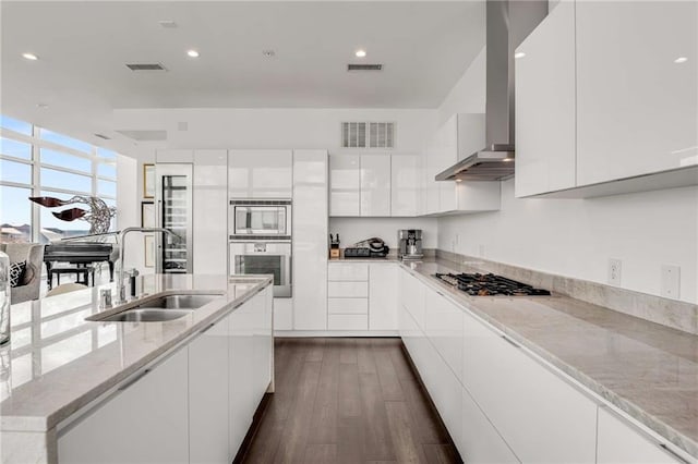 kitchen featuring range hood, stainless steel gas stovetop, white cabinetry, sink, and light stone counters