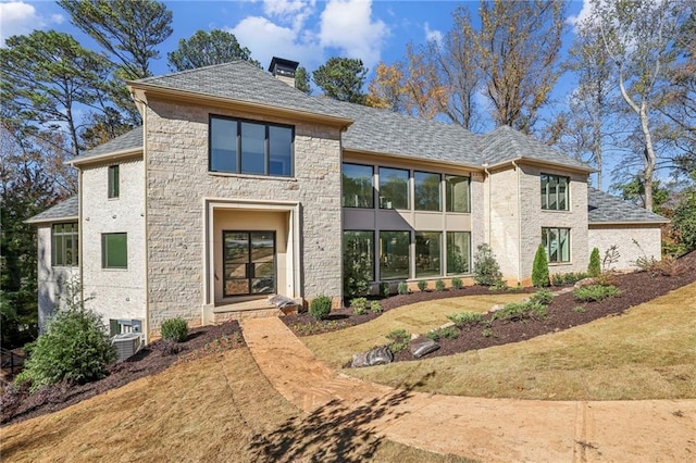 view of front of house featuring a chimney, stone siding, a shingled roof, and central AC