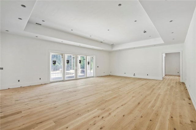 unfurnished living room with a tray ceiling, light wood-style flooring, and baseboards