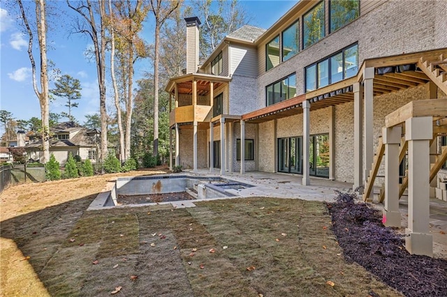 back of property featuring a chimney, a patio, a balcony, brick siding, and an empty pool