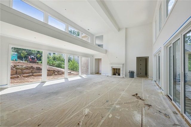 unfurnished living room with a high ceiling, a wealth of natural light, and beam ceiling