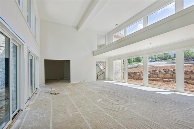 unfurnished living room featuring a towering ceiling and beam ceiling