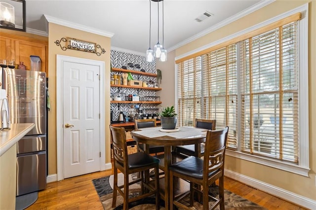 dining area featuring visible vents, a bar, crown molding, light wood finished floors, and baseboards