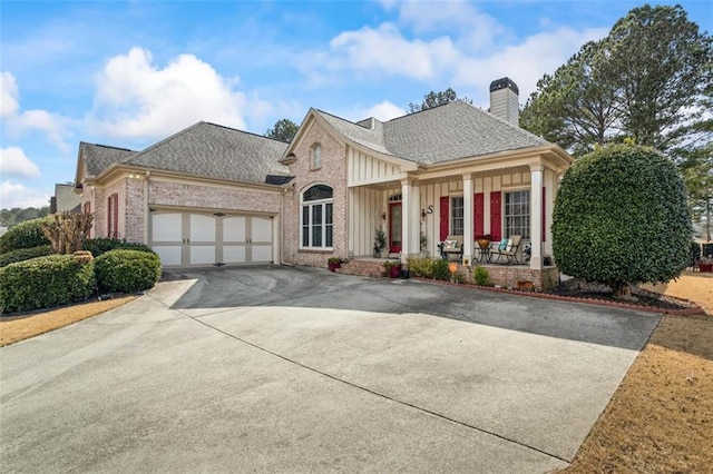 view of front of home featuring brick siding, a porch, a chimney, a garage, and driveway