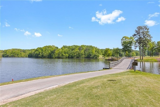 view of dock featuring a lawn, a water view, and a view of trees