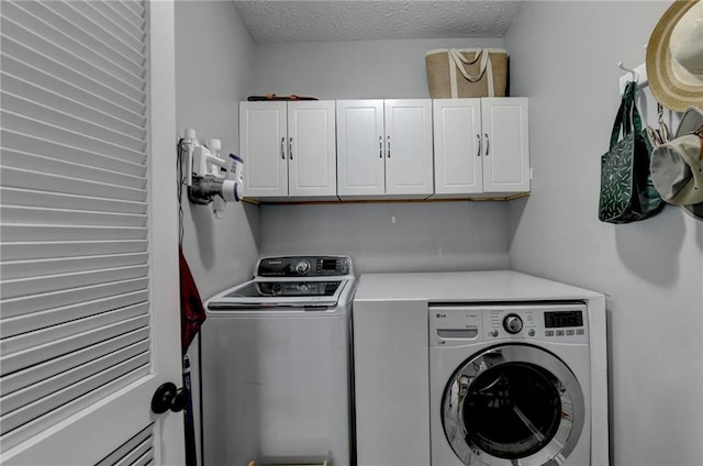 washroom featuring cabinets, a textured ceiling, and washer and clothes dryer