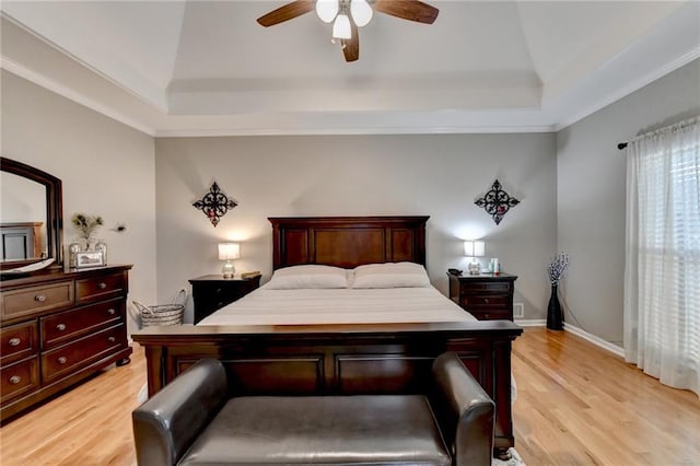 bedroom featuring a raised ceiling, ceiling fan, crown molding, and light wood-type flooring