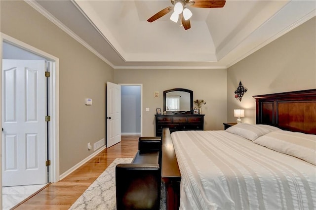 bedroom featuring crown molding, a raised ceiling, ceiling fan, and light wood-type flooring