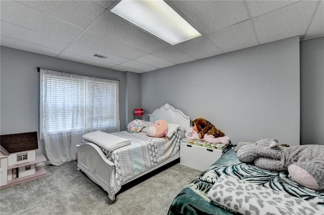 bedroom with a drop ceiling and light colored carpet