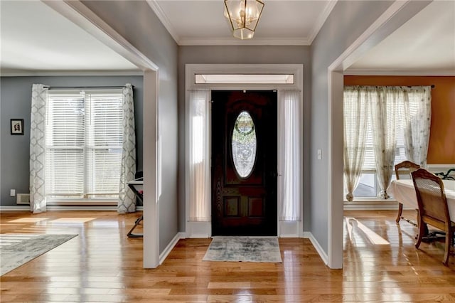 foyer with ornamental molding, a notable chandelier, and light hardwood / wood-style floors