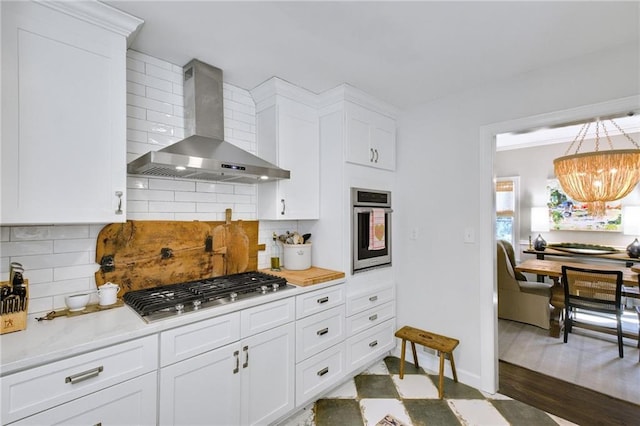 kitchen with wall chimney range hood, backsplash, white cabinets, and appliances with stainless steel finishes