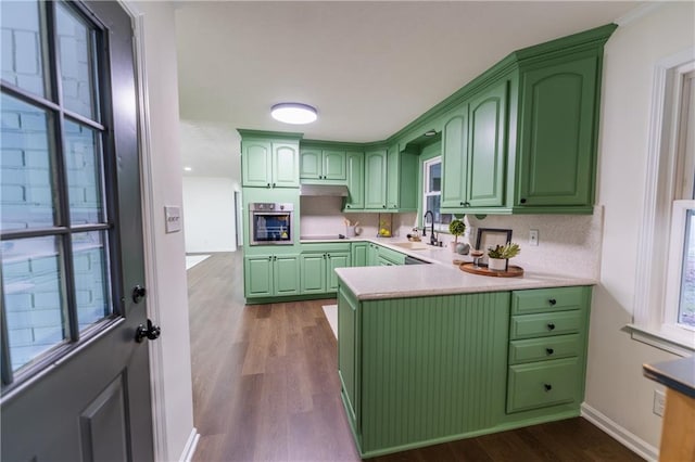 kitchen featuring wood finished floors, a sink, stainless steel oven, green cabinets, and light countertops