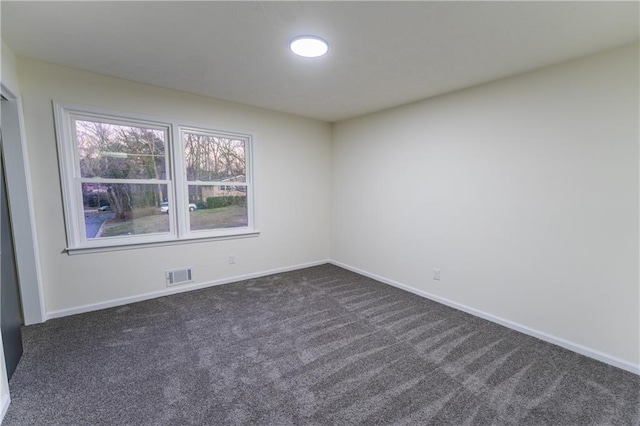 empty room featuring dark colored carpet, visible vents, and baseboards